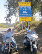 While seated on their motorcycles, three drivers point to the new motorcycle sign "Caution Next 12 Miles. Since Jan 2006 10 Killed in Motorcycle related crashes. Stay Alert. Save a life."s.