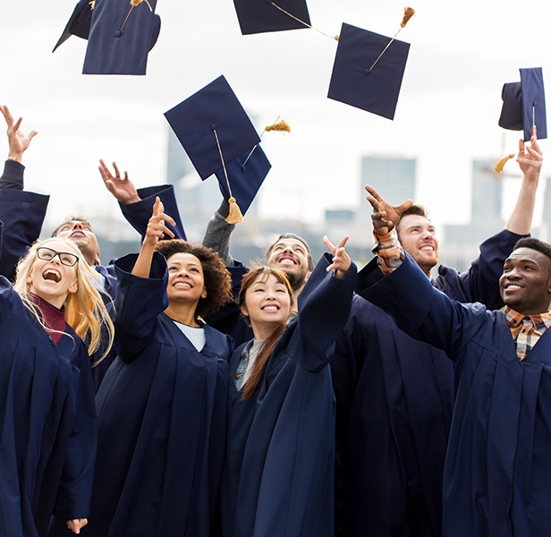 Diverse group of college graduates in cap and gowns throwing caps in air with city in background