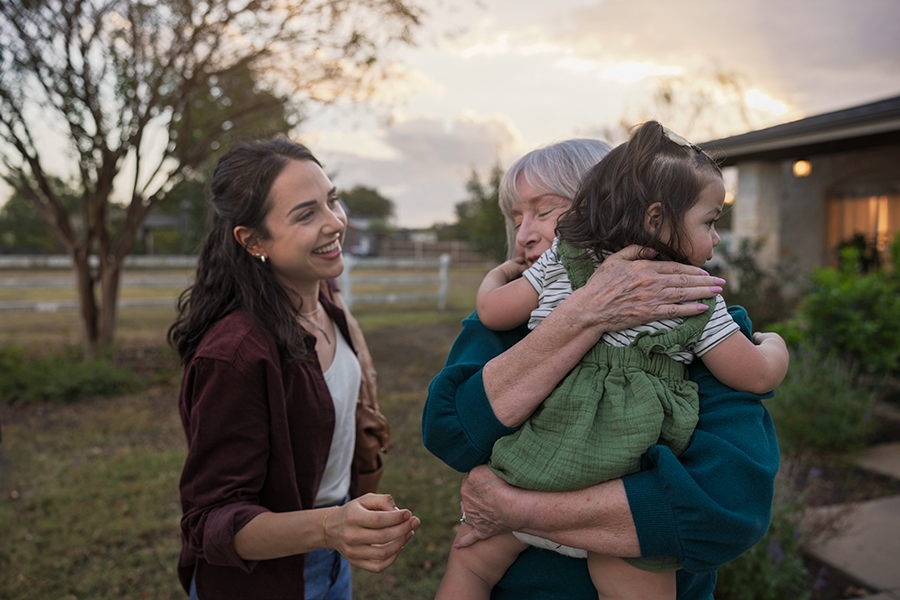 Older adult female holding child in front of house