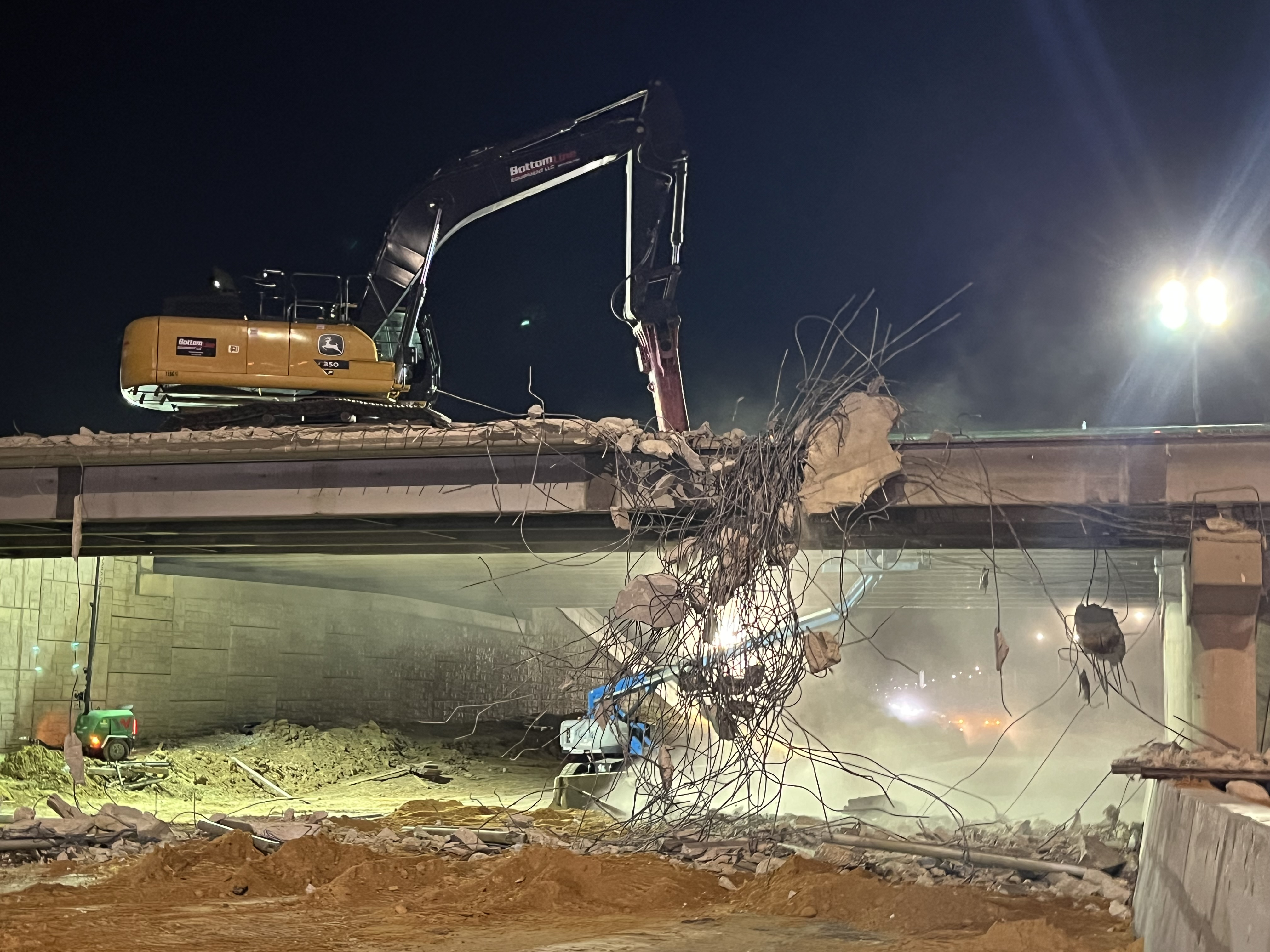 #1 Lake June bridge Dallas A machine with a claw atop the Lake June bridge is reaching into a tangle of metal wires that are coming out of the bridge in the middle of the construction site at night.