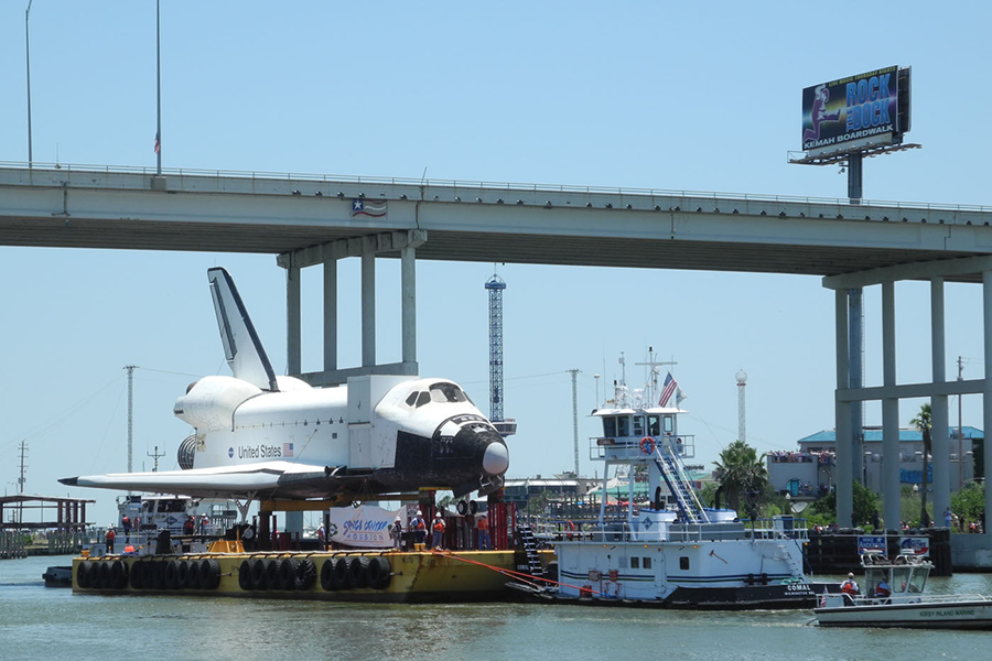 Space shuttle on a barge passing underneath a bridge