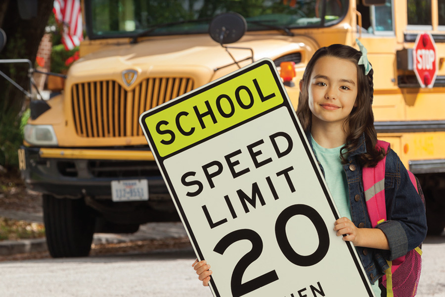 Joven estudiante sosteniendo una señal de límite de velocidad escolar frente al autobús estacionado
