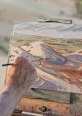 Close-up of an artists hand painting a desert scene