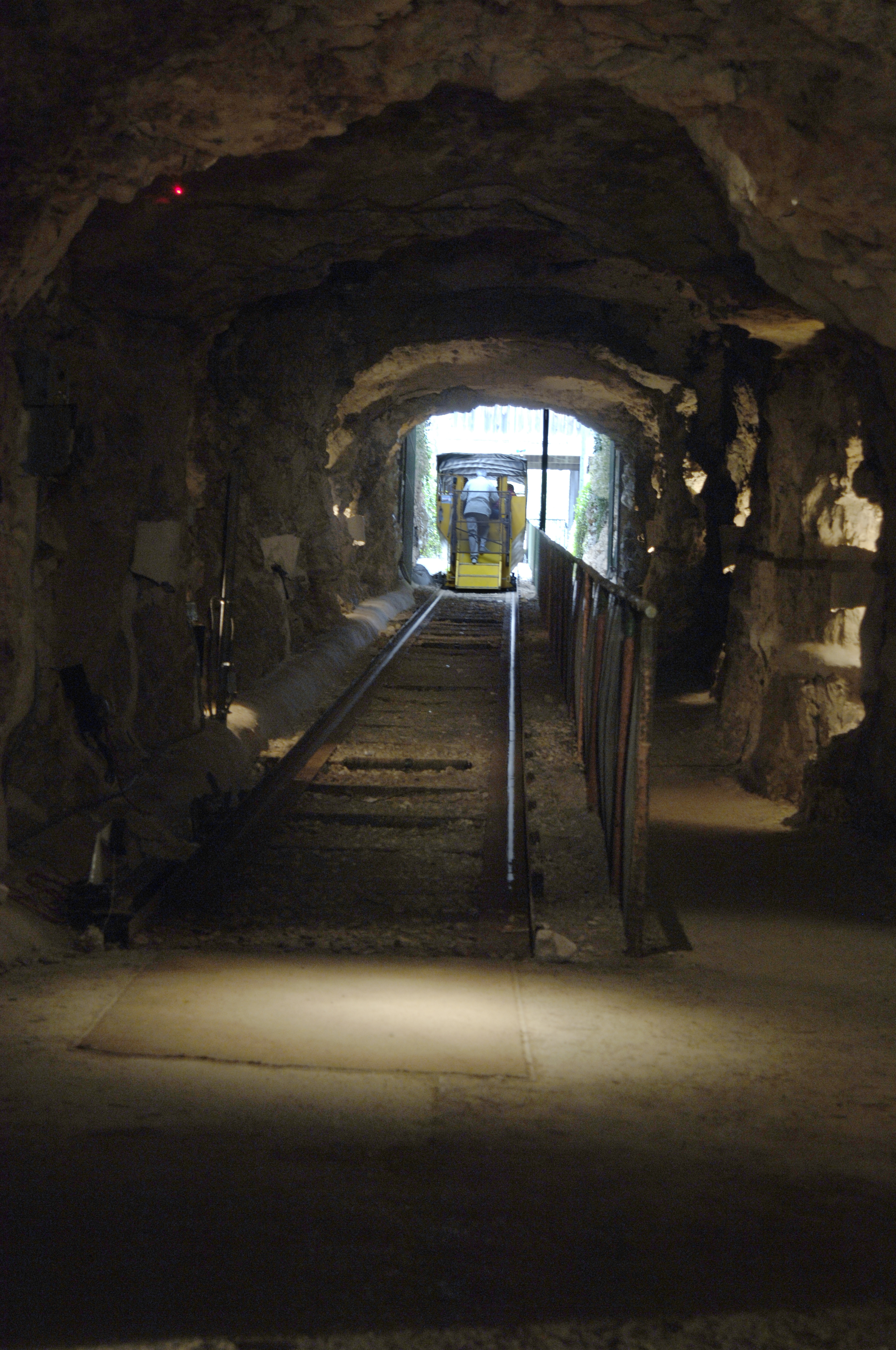 A photo of rail tracks through an underground stone tunnel at Inner Space Cavern with light and a small open air train with passengers on it visible at the end of the tunnel. 