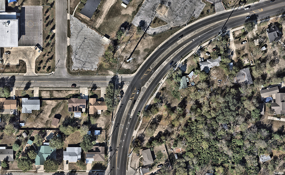 Aerial view of a Continuous Green‑T (CGT) intersection at Thunder Drive and Callaghan Road, showing a three‑leg layout where the curved major roadway maintains uninterrupted through traffic while the side street connects via dedicated turn lanes.