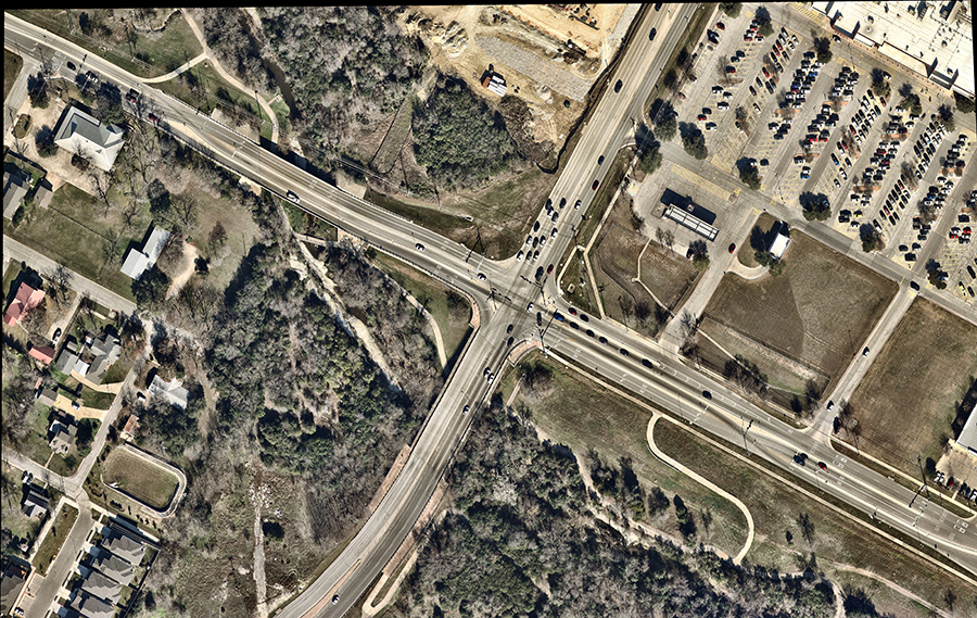 Aerial view of a displaced left-turn (DLT) intersection showing left-turn vehicles crossing opposing traffic at upstream signalized crossovers before reaching the main intersection, enabling simultaneous through and left-turn movements across the intersection.