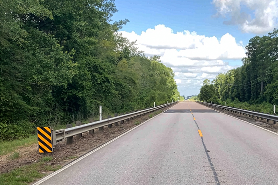 A rural roadway with guardrails and culvert.