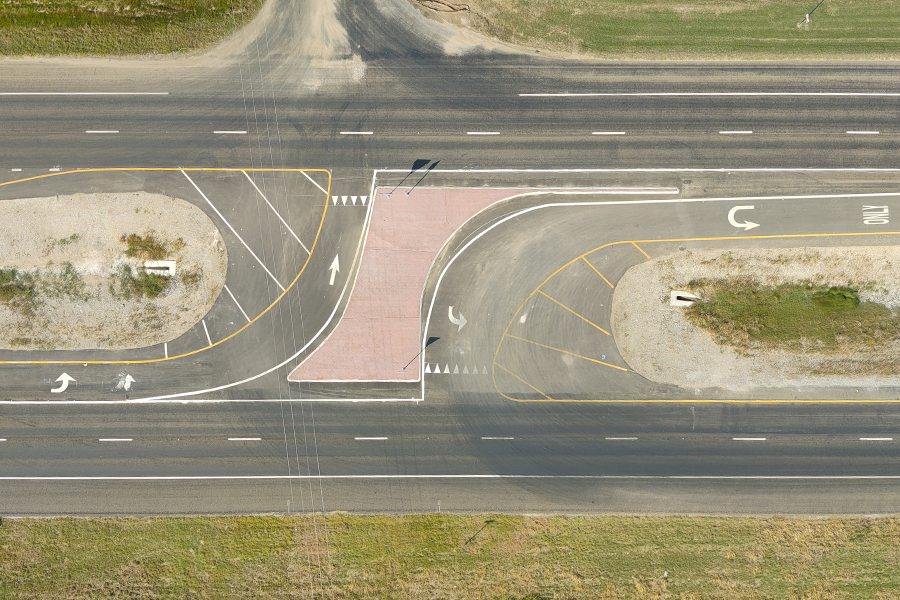 A top-down view of restricted crossing U-turn featuring traffic markings, directional arrows, and two large grassy traffic islands. Includes designated left- and right-turn lanes.