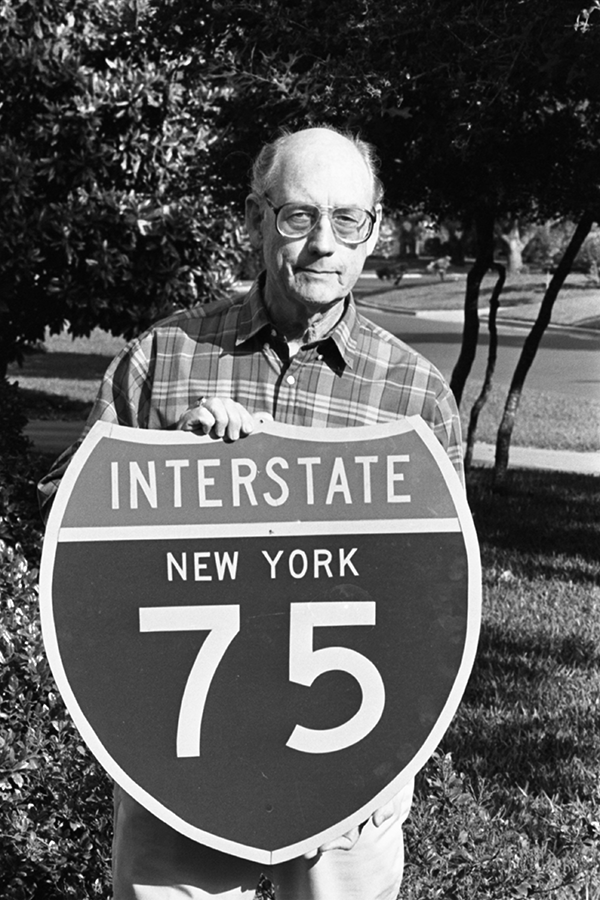 Foto negra y en blanco del empleado de TxDOT Richard Oliver sosteniendo un cartel de escudo para la Interestatal 75.