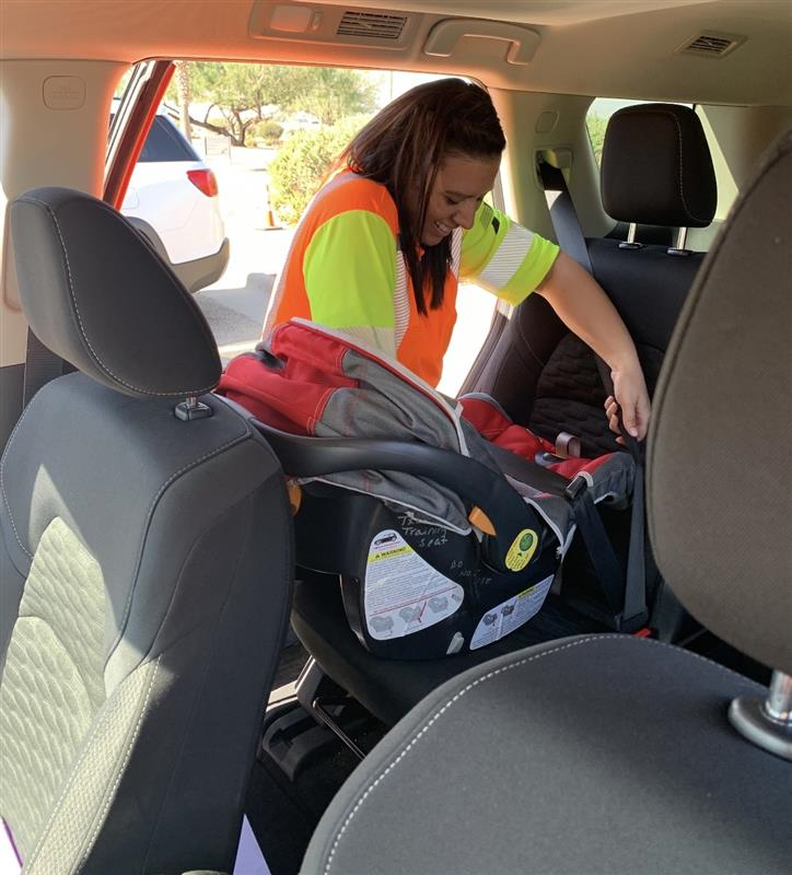 Una mujer con un chaleco de seguridad instala un asiento de seguridad en un vehículo.