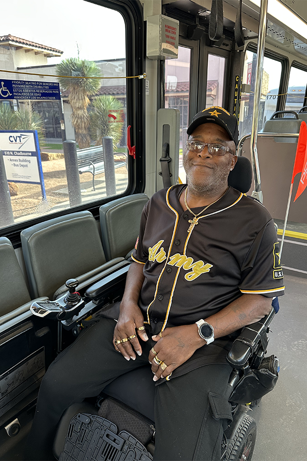 A man in an assistive wheelchair smiles as he rides a public bus.