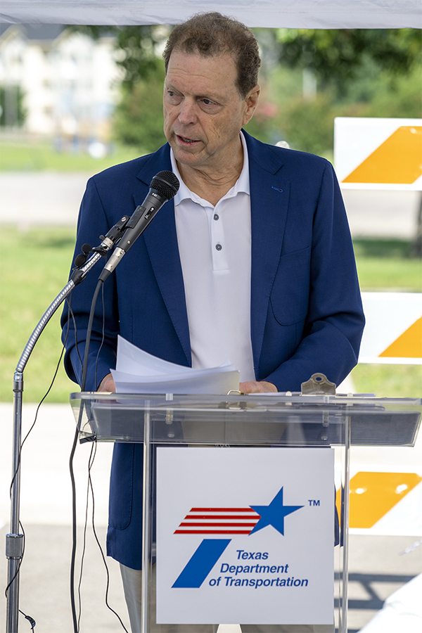 Texas Transportation Commissioner Vaughn speaking at a lectern at Spur 399 groundbreaking ceremony.