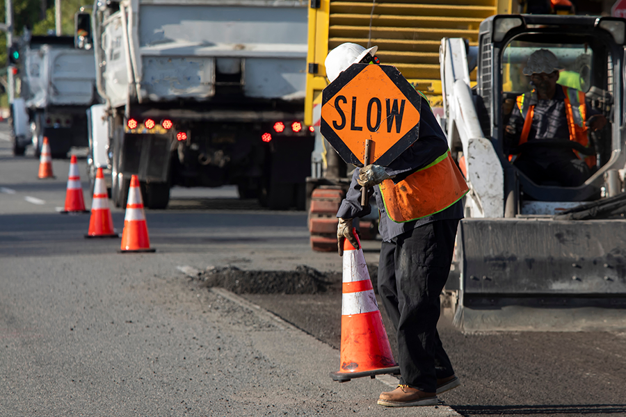 Trabajador de la construcción de carreteras sostiene un cartel de reducción de velocidad