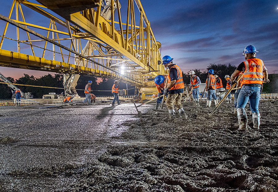 Road construction worker pouring concrete at night