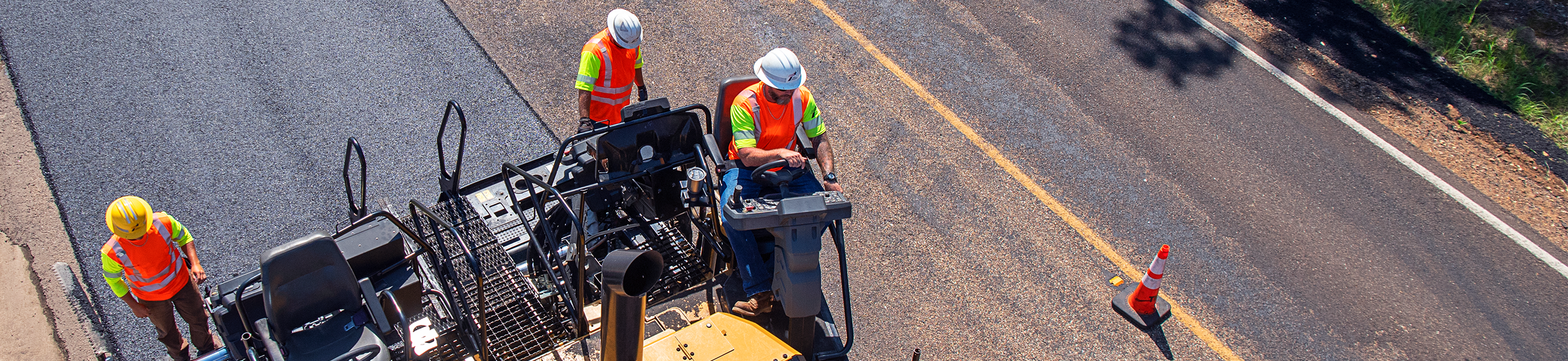 Tres trabajadores de mantenimiento de carreteras de TxDOT agregan superposición a la carretera vista desde arriba