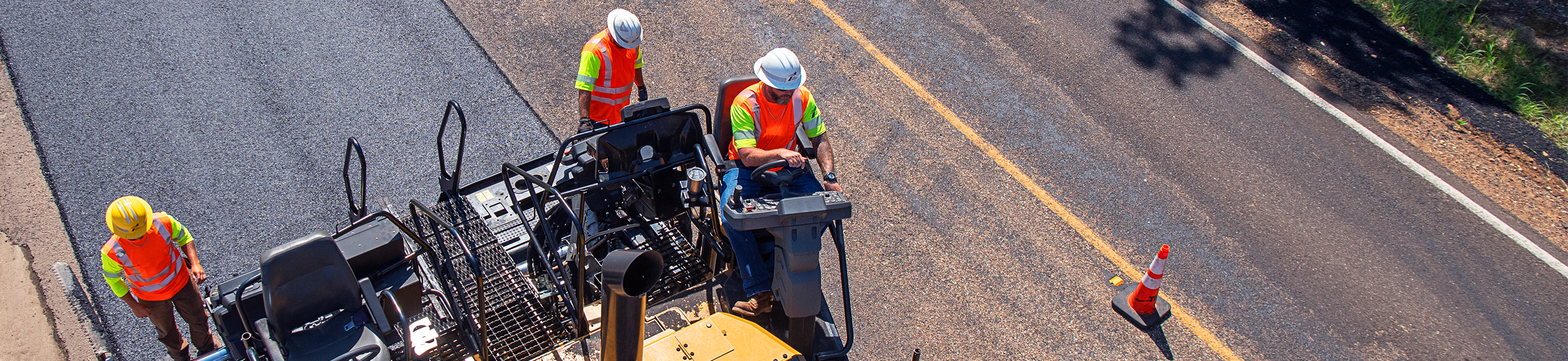 Three TxDOT road maintenance workers adding overlay to road viewed from above