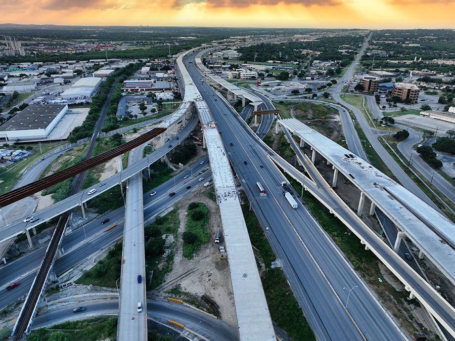 Aerial view of the I-35 and Loop 410 interchange in San Antonio, showing multiple elevated flyover ramps under construction, active highway traffic, and ongoing improvements to expand regional mobility.