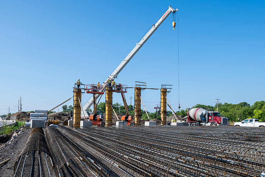 Trabajadores de TxDOT en la parte superior de un pilar amarillo en un sitio de construcción