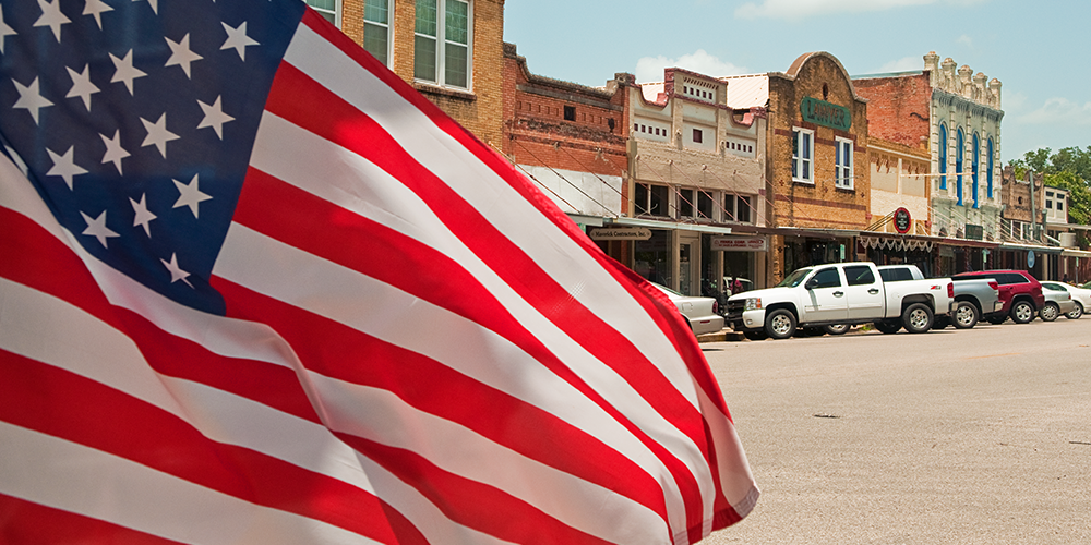 US flag waving on street in columbus Texas with cars in background