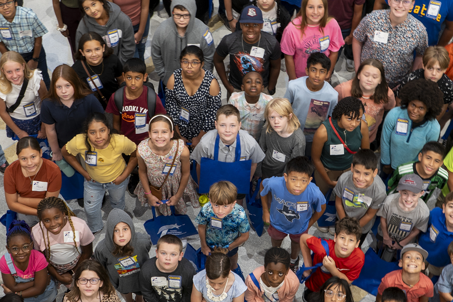 Elementary school students visiting TxDOT Headquarters, posing indoors with staff in high-visibility vests.