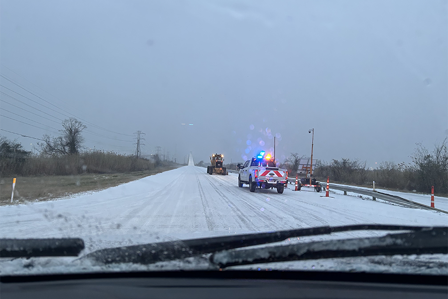 TxDOT work trucks on snowy road, seen through vehicle windshield