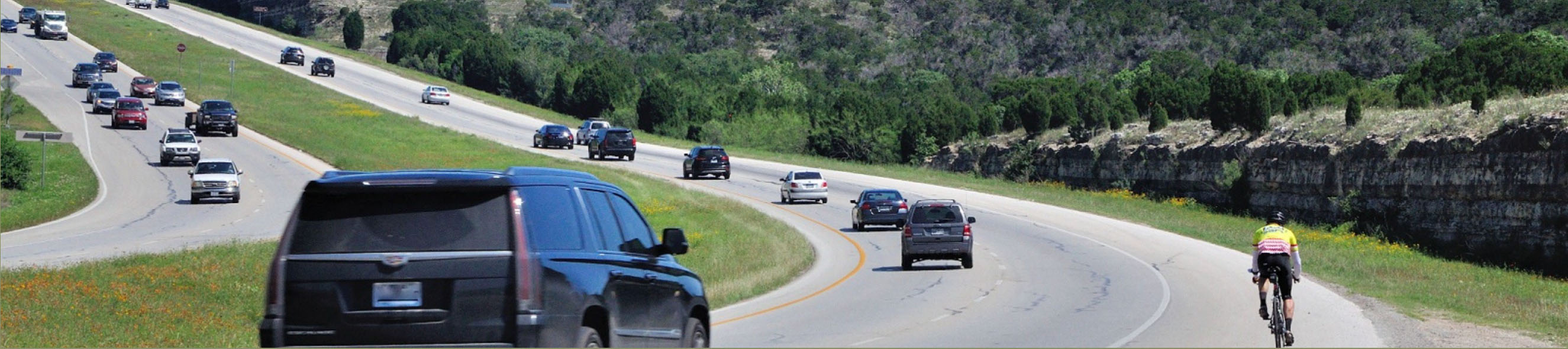 Northbound Loop 360 traffic with a bicyclist riding along in the shoulder of the road