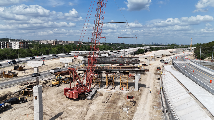 Una grúa coloca cuidadosamente una jaula de tapa de barra de refuerzo en columnas recién terminadas para una parte de un puente de rampa cerca del intercambio "Y". En la configuración final, los conductores podrán usar este puente para llegar a la US 290 desde la SH 71 después de pasar por un Intercambio Urbano de Punto Único.  Mayo 2025