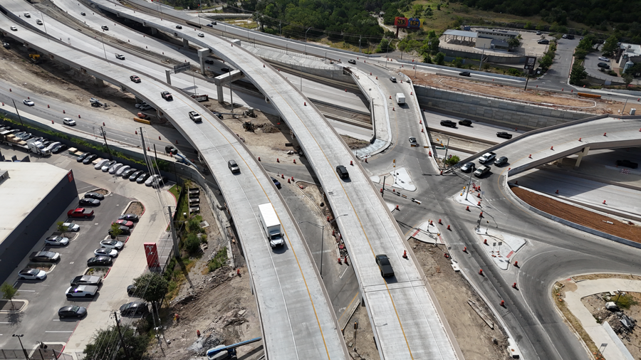 Overhead view of US 290 at SH 71 looking south, with single-point urban interchange (SPUI) carrying local traffic and mainlane flyovers overhead. July 2026.
